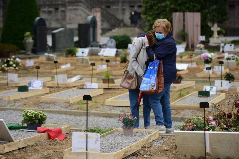 Relatives of a deceased person comfort themselves at the Monumental Cemetery of Bergamo, Lombardy, a day after it reopened on May 19, 2020 as the country's is easing its lockdown aimed at curbing the spread of the COVID-19 infection, caused by the novel coronavirus. - A new area in the cemetery of Bergamo is being dedicated to some of the people who have died in recent weeks and who have expressly asked to be buried in the ground and not cremated, and who do not have a family tomb or burial place. (Photo by Piero CRUCIATTI / AFP) (Photo by PIERO CRUCIATTI/AFP via Getty Images)