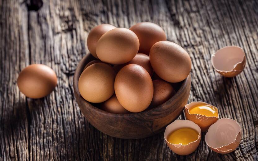 Chicken eggs in wooden bowl on rustic oak table